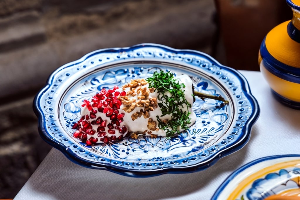 Traditional Chiles en Nogada features walnut cream sauce, vibrant pomegranate seeds, and fresh parsley leaves.