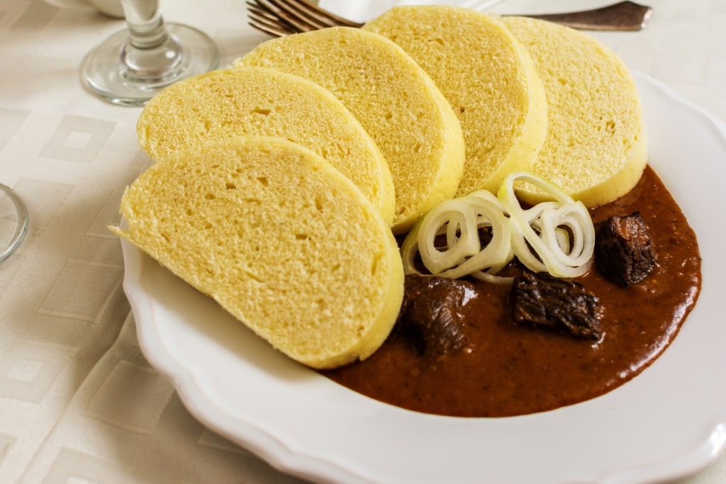 A hearty plate of traditional Czech beef guláš served with fresh onions and soft bread dumplings.