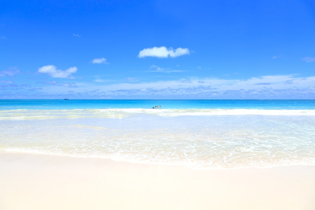 Pristine Kailua-Kona sand shoreline framing calm, translucent, turquoise, tropical resort ocean waters.
