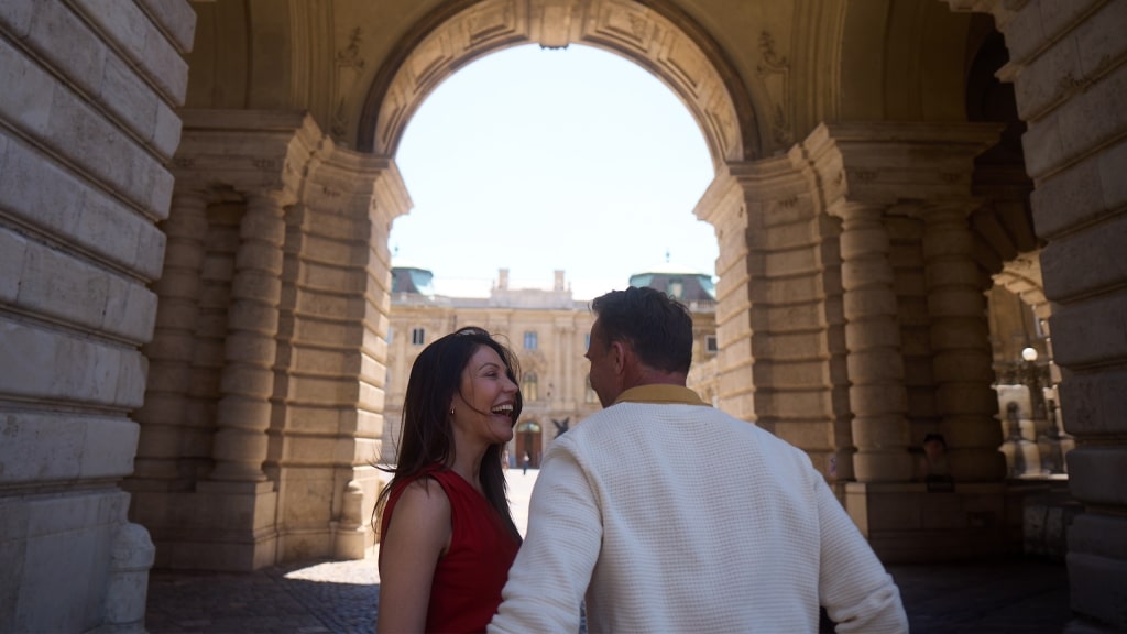 A couple shares a joyful laugh framed by a majestic stone archway in Budapest.