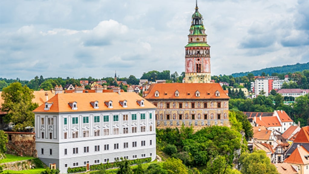 The colorful tower of Český Krumlov Castle rises gracefully above historic orange-roofed buildings.