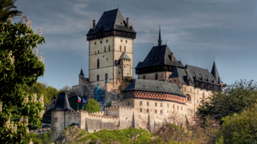 Karlštejn Castle’s imposing stone towers and fortified walls rise high above a lush hillside.