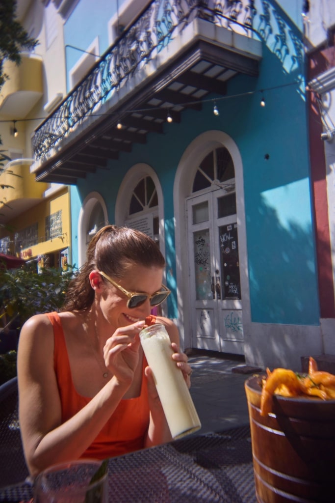 A smiling woman holds a piña colada on the historic streets of San Juan.