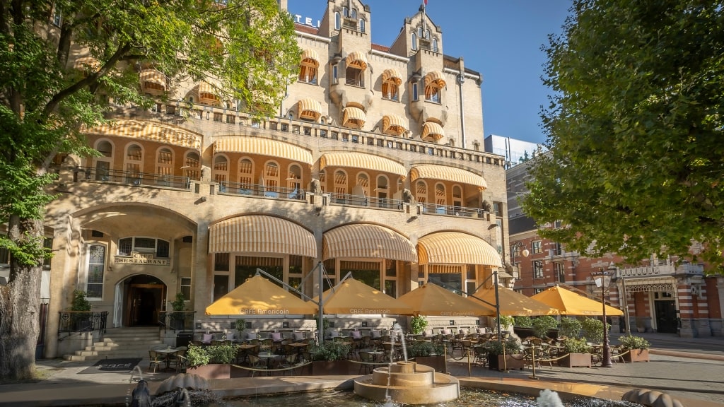 Yellow umbrellas and a fountain frame the grand facade of Clayton Hotel Amsterdam American.