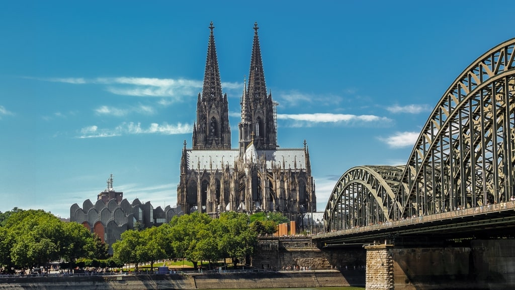 Cologne Cathedral’s towering twin spires rise majestically behind a massive arched bridge.