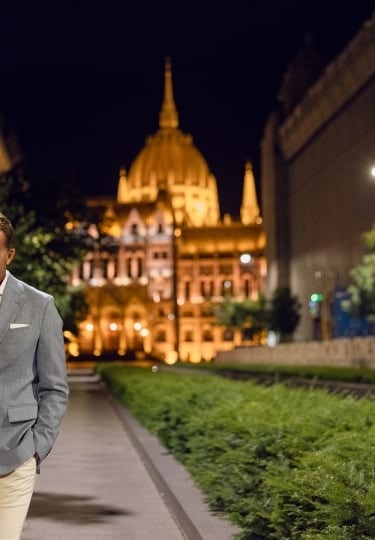 A couple shares a warm smile while strolling at night before the illuminated dome of the Hungarian Parliament Building.