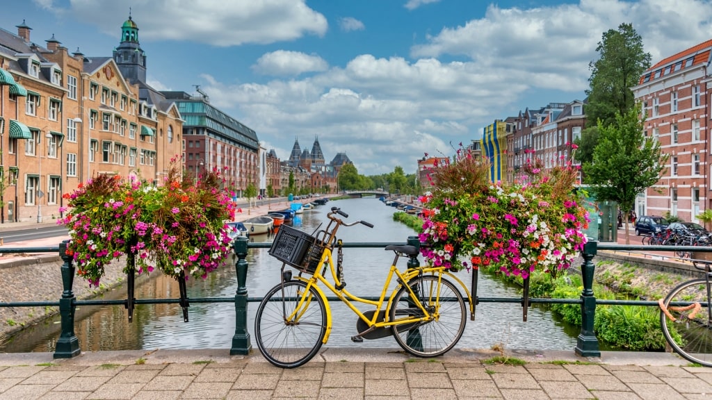 Vibrant flowers and a yellow bicycle on a bridge overlooking an Amsterdam canal.