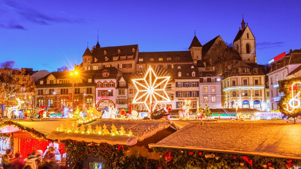 A giant glowing star illuminates festive market stalls in Basel under a twilight sky.