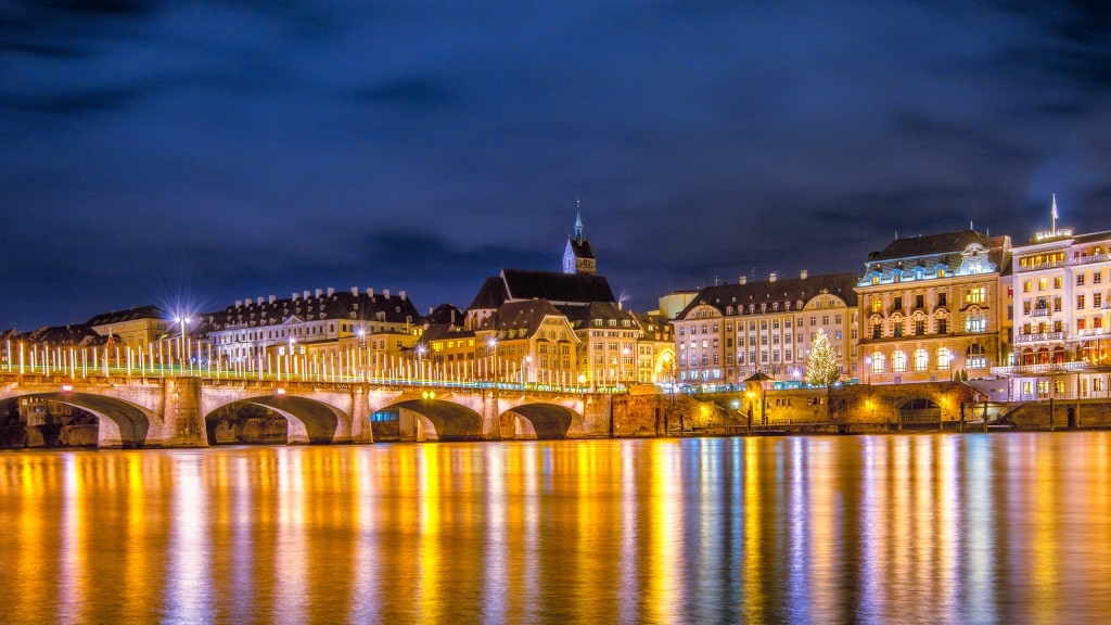 The illuminated Mittlere Brücke casts brilliant golden reflections across the dark Rhine River.