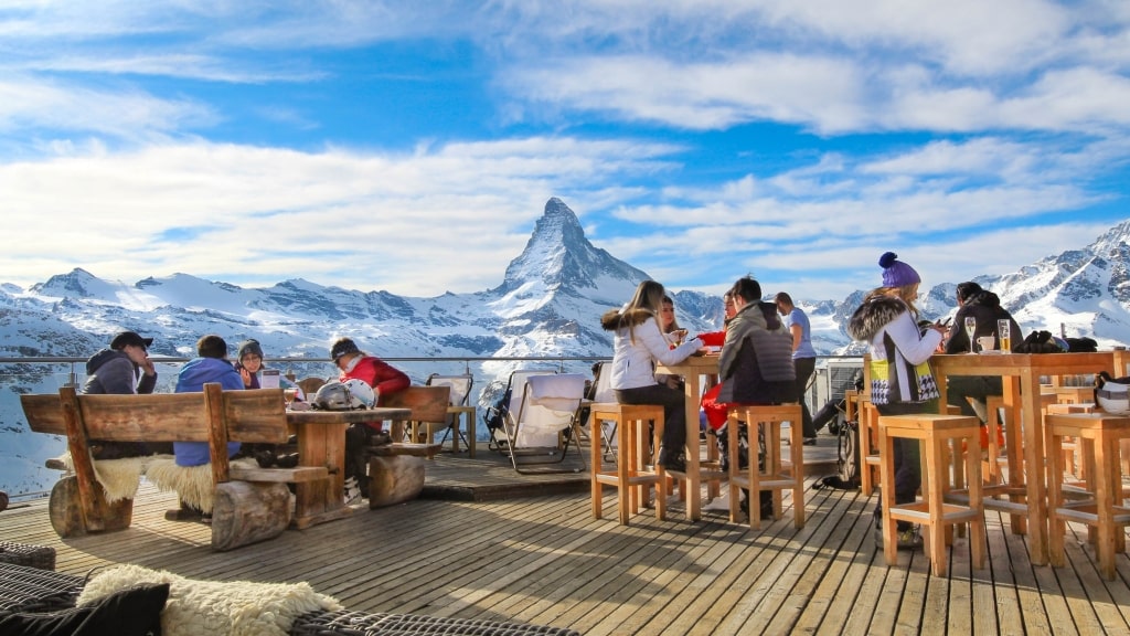 Outdoor dining tables face the striking, snow-dusted peak of the Matterhorn under blue skies