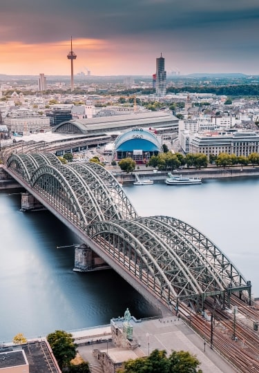 An aerial view of a bridge over the Rhine River with the Majestic Cologne Cathedral in the background.