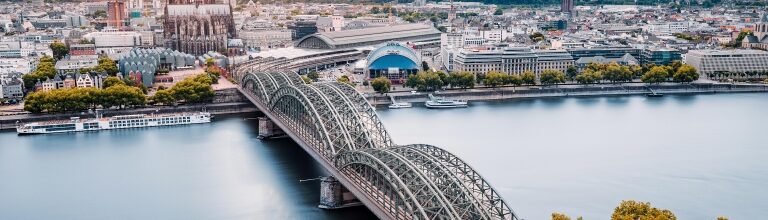 An aerial view of a bridge over the Rhine River with the Majestic Cologne Cathedral in the background.