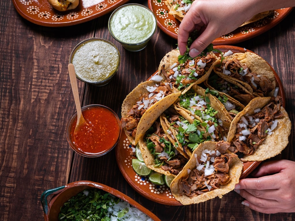 Traditional tacos al pastor topped with fresh cilantro and diced onions served alongside vibrant salsas.