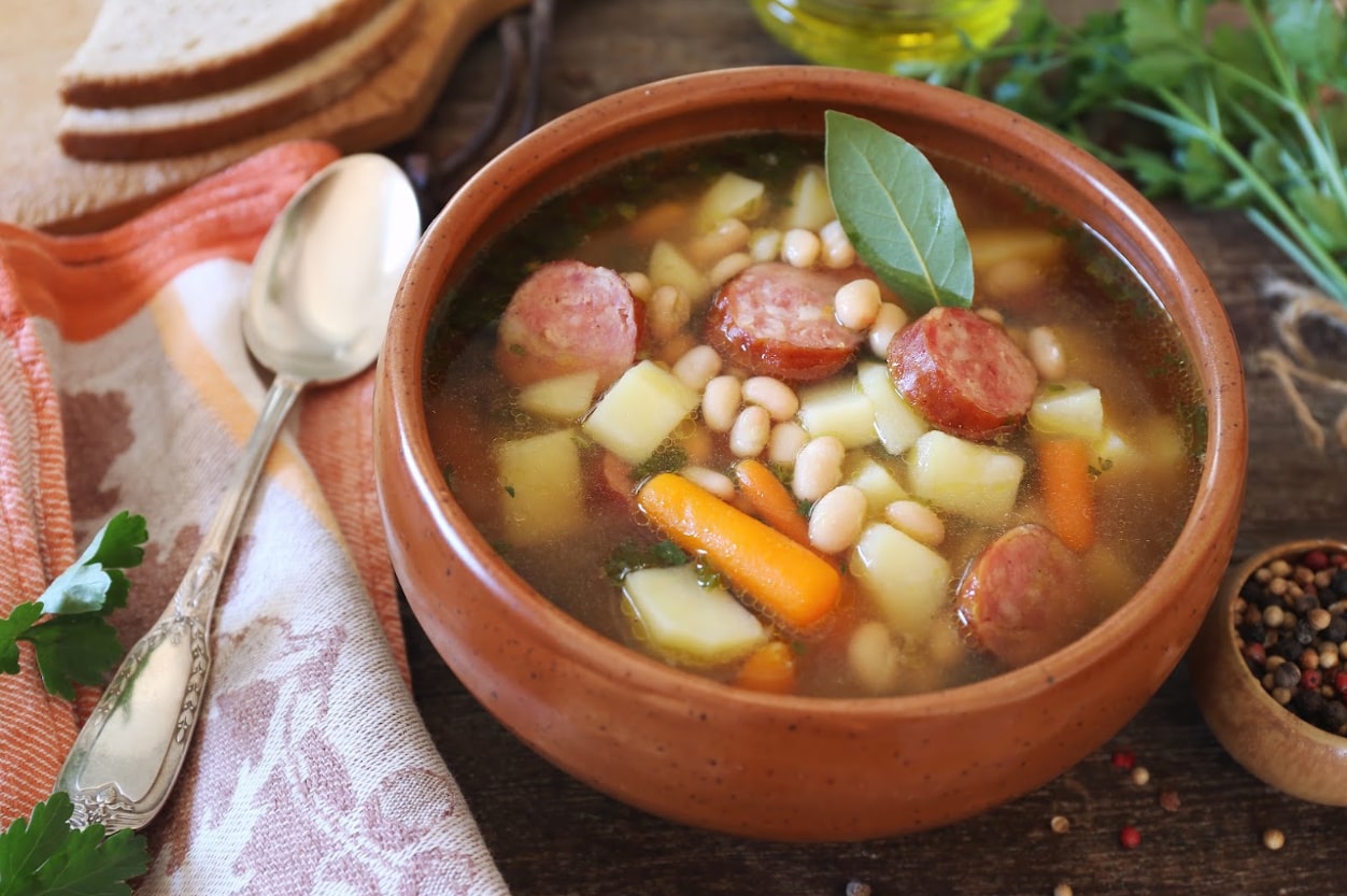 A traditional Galician broth, Caldo Gallego, is presented in a classic clay bowl, brimming with beans, greens, and savory sausage.