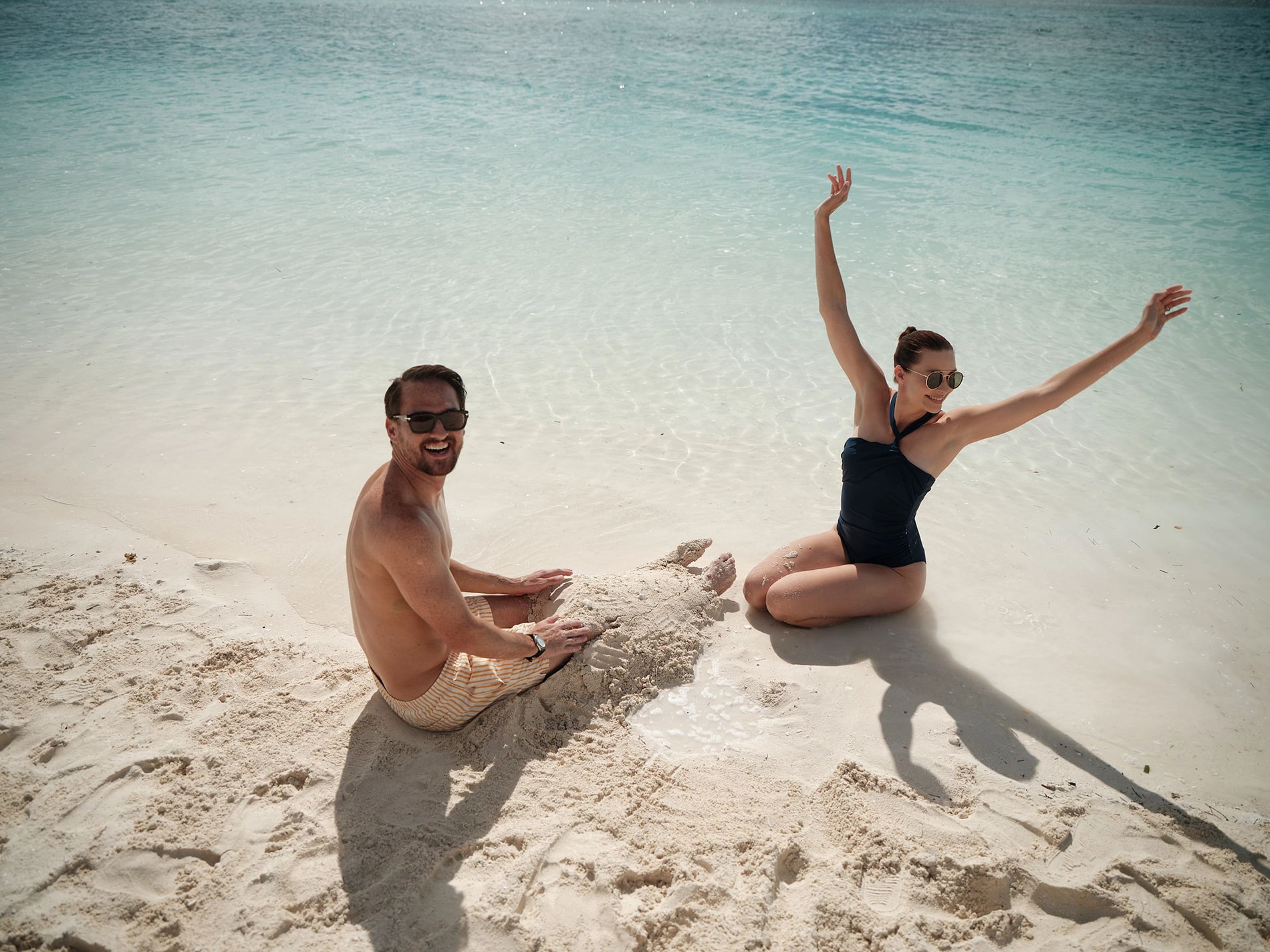A joyful couple shares a playful moment on the sun-drenched sands of a Bahamian paradise.