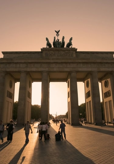 Bathed in a warm, golden glow, the legendary Brandenburg Gate presides over the square in Berlin while walkers leave long shadows in their wake.