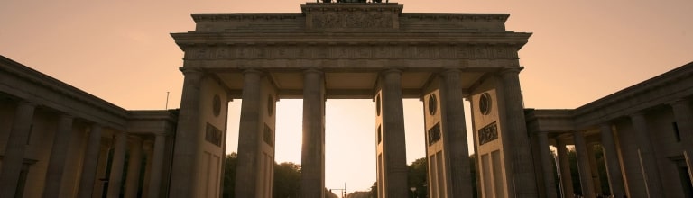 Bathed in a warm, golden glow, the legendary Brandenburg Gate presides over the square in Berlin while walkers leave long shadows in their wake.
