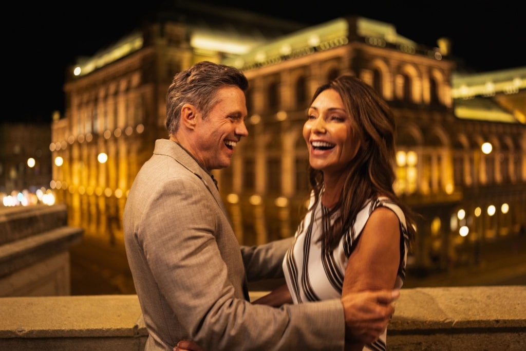 An elegant pair sharing a moment by the glowing Vienna State Opera after sunset.