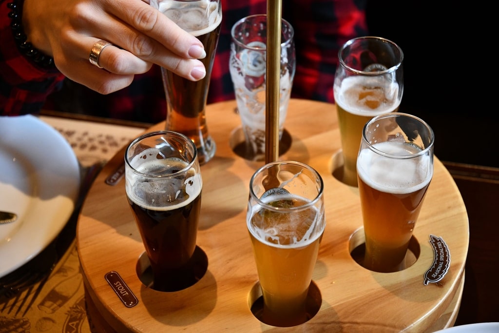 A wooden flight displays various craft beers, including stouts, lagers, and ales.