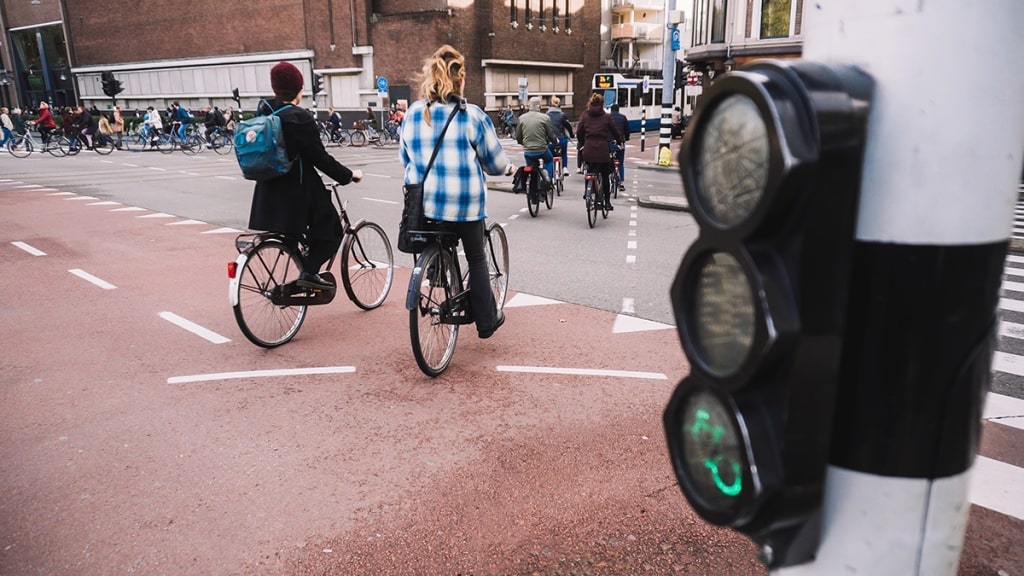 A group of cyclists navigates an urban junction, as a dedicated traffic light illuminates a glowing green bicycle icon in Amsterdam.