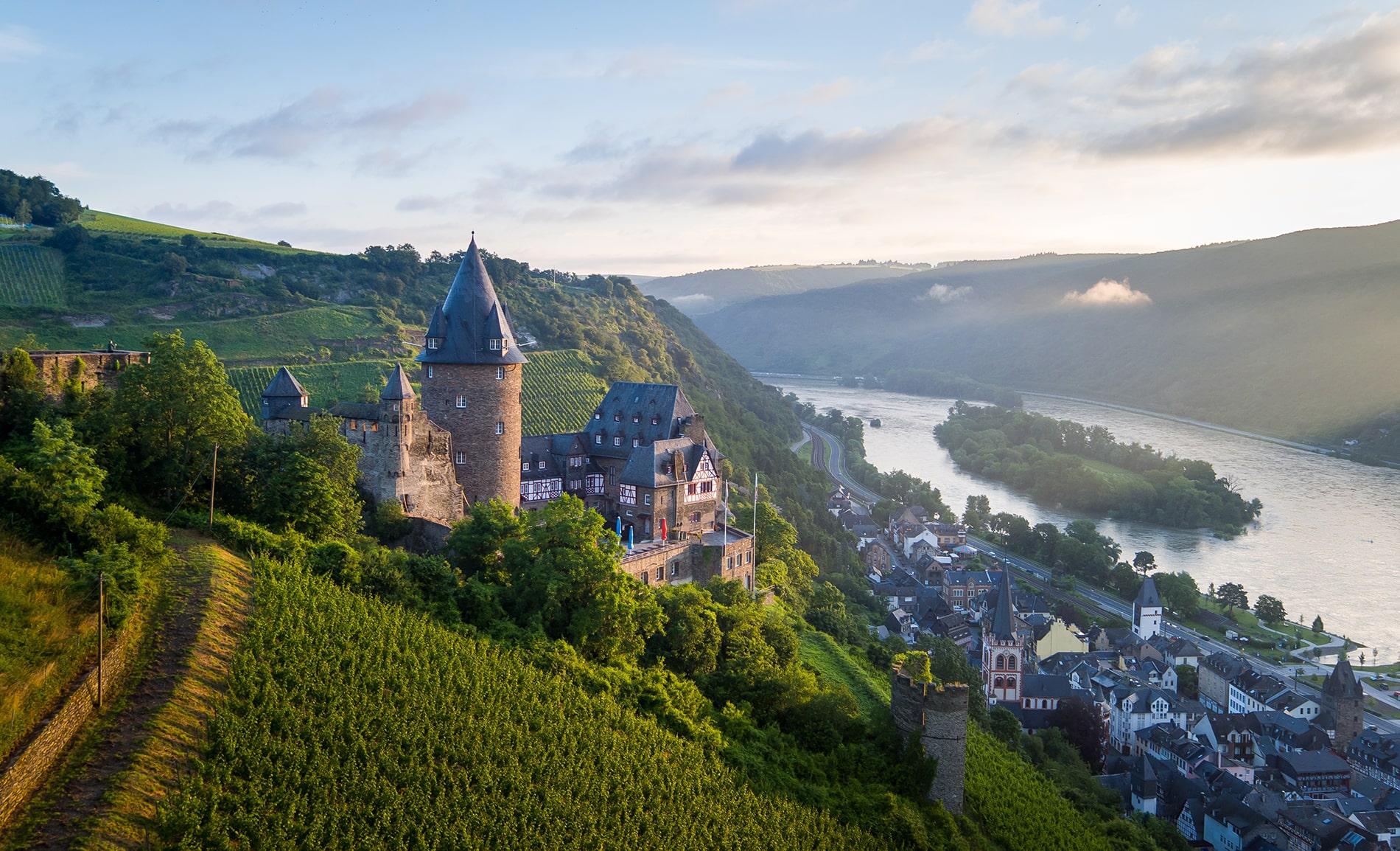 Burg Stahleck stands on a lush hillside, overlooking the town of Bacharach and the winding Rhine River.