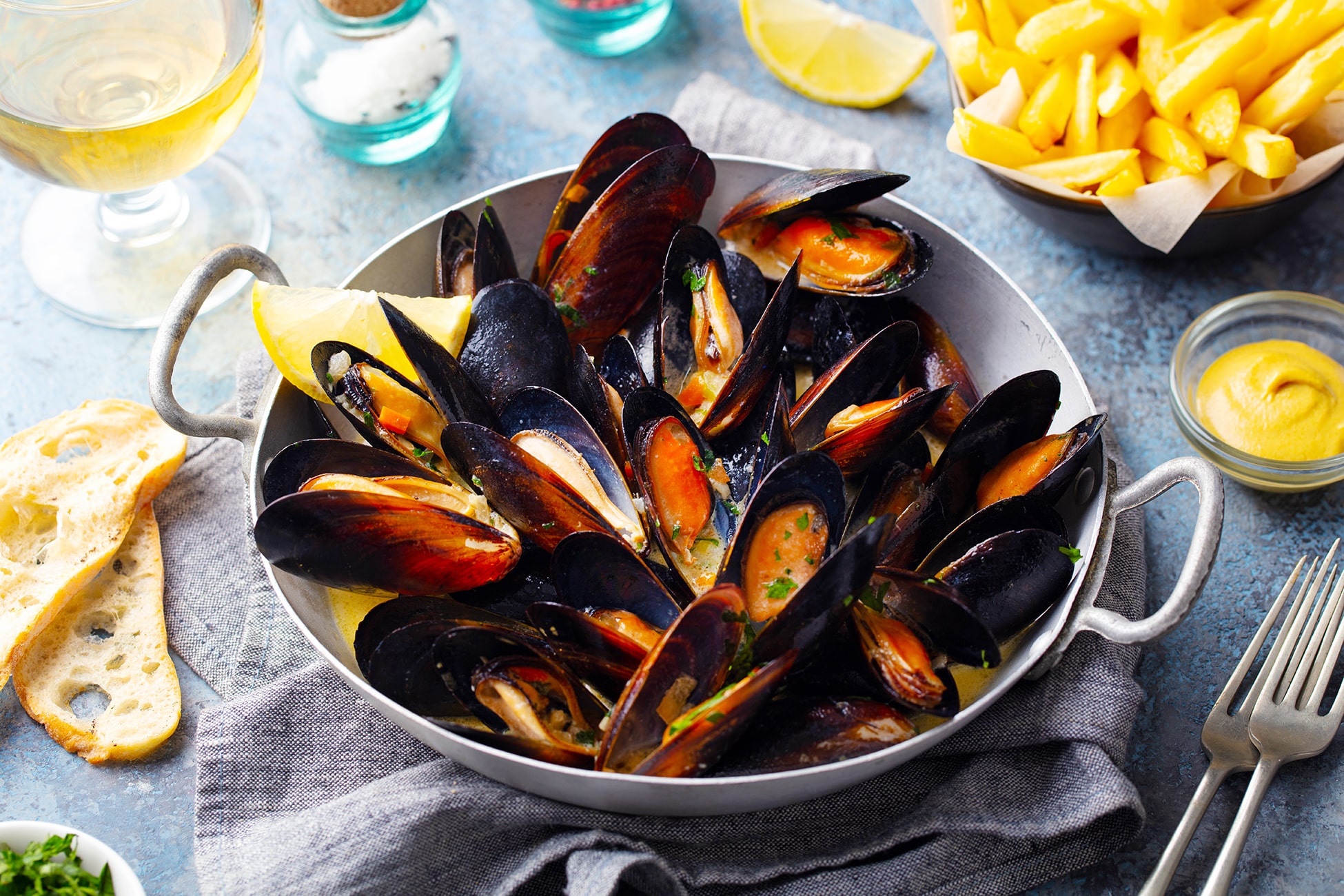 Mussels with french fries and white wine in cooking pan. Grey background. Close up.