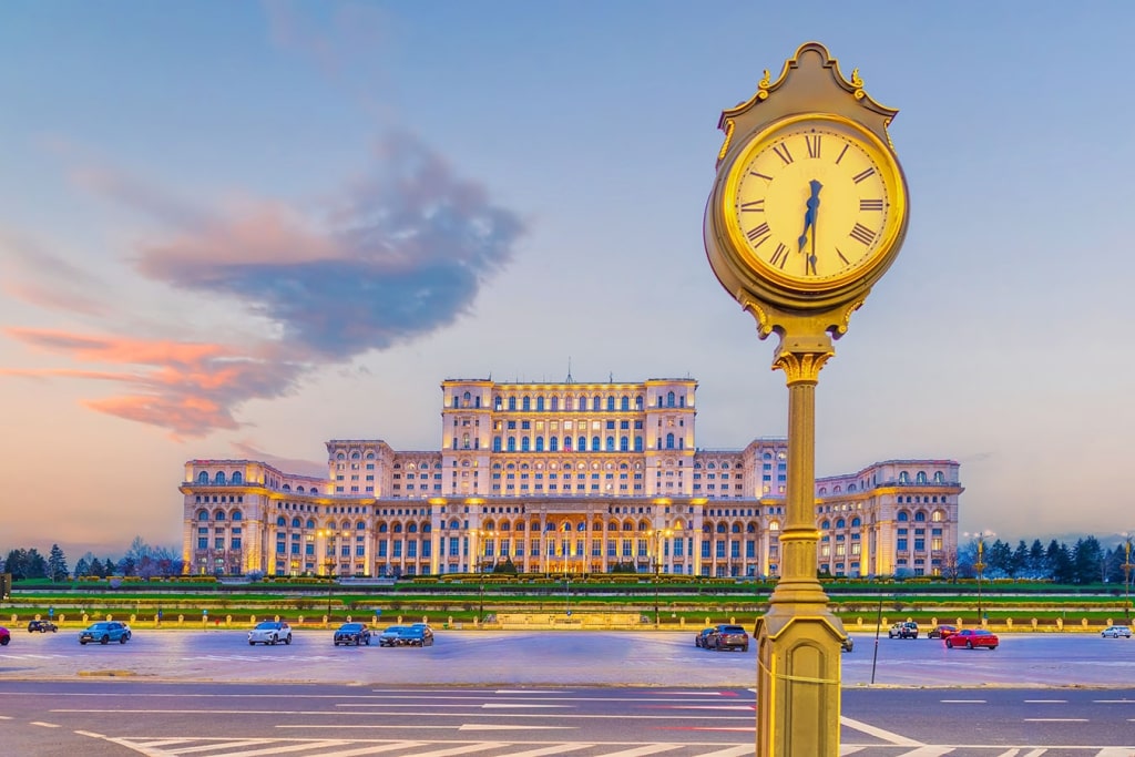 The Palace of the Parliament in Bucharest, Romania, viewed at sunset with a historic street clock in the foreground.