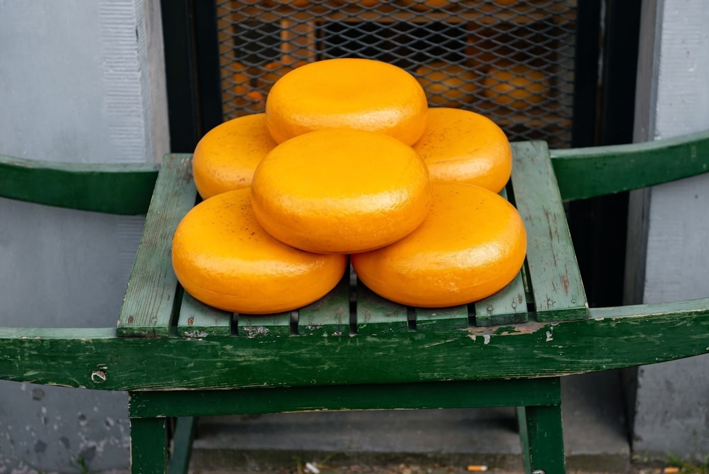 Lustrous wheels of traditional Gouda, glowing in vibrant shades of orange and gold, arranged atop a rustic green wooden barrow for display.