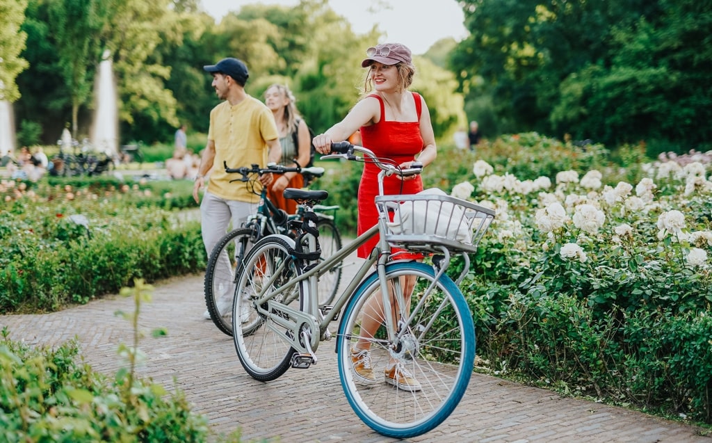 A cheerful traveler strolls with her bicycle, enjoying the blossoming floral path alongside her friends.