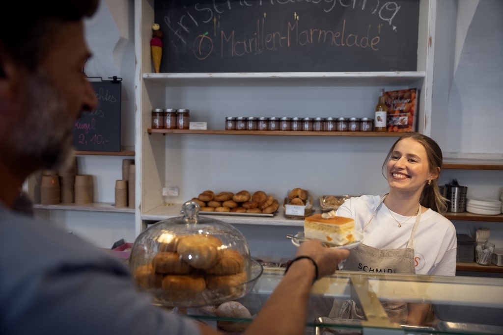 A warm exchange over a slice of cake in a local bakery illustrates how small, cash-in-hand transactions build intimate connections with the faces behind Europe’s culinary traditions.