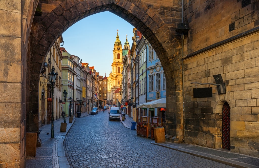 A stone arch frames cobblestone streets and Baroque architecture in Malá Strana.