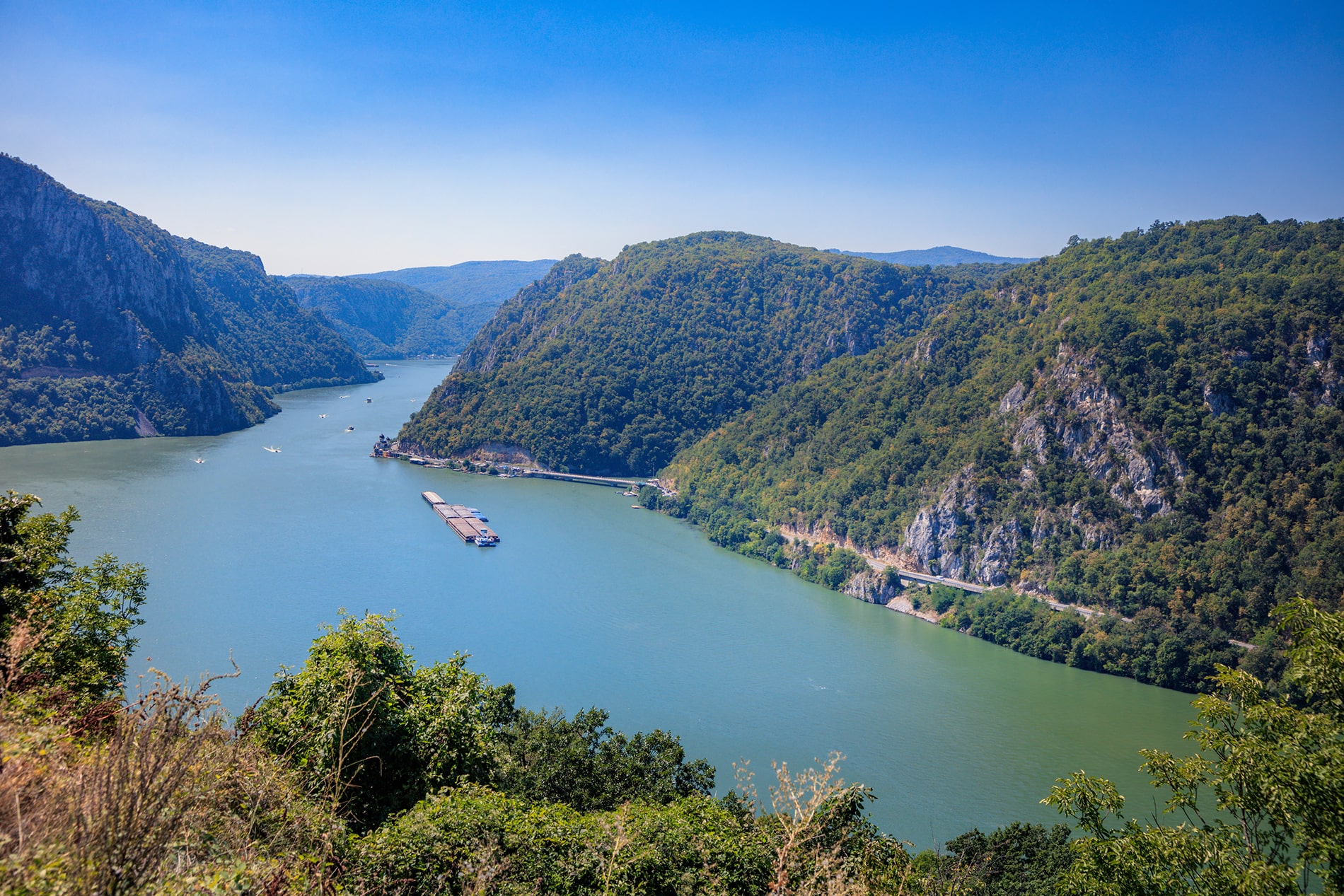 The Danube River carves a dramatic blue path through towering, forest-covered limestone cliffs in Serbia's Iron Gate Gorge