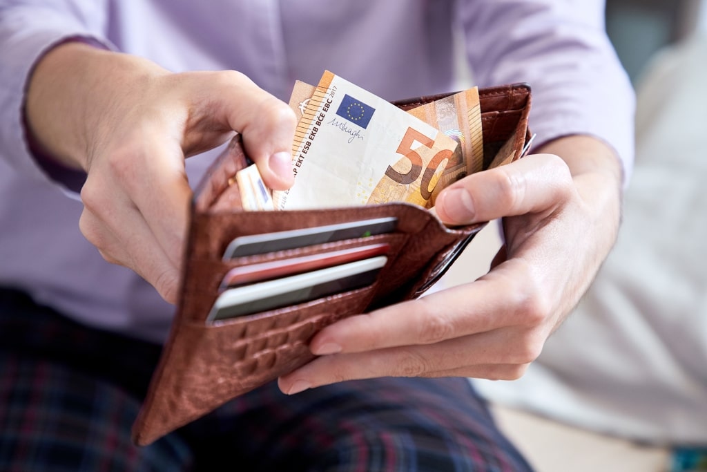 Hands slip a crisp 50 Euro (€) note into a leather wallet—a quiet, tactile moment of shore-day prep before stepping off the ship onto historic European ports.