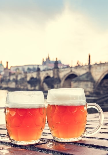 Against the backdrop of Prague's historic Charles Bridge and the amber hues of twilight, two glasses of crisp, bottom-fermented Czech lager rest prominently at a Vltava riverfront tavern.