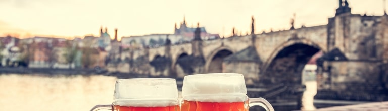 Against the backdrop of Prague's historic Charles Bridge and the amber hues of twilight, two glasses of crisp, bottom-fermented Czech lager rest prominently at a Vltava riverfront tavern.