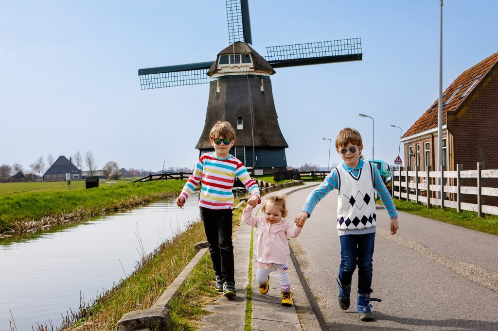 Children walking hand-in-hand past a traditional windmill capture the joyful, family-friendly side of exploring the Dutch countryside.