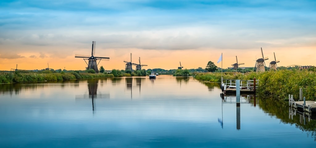 Reflecting across glassy waters under a soft dusk sky, the iconic windmills of Kinderdijk set a serene scene along the river.