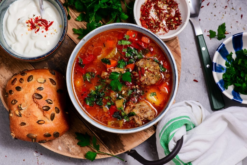 Hearty Romanian ciorbă de perișoare meatball soup served with fresh bread.