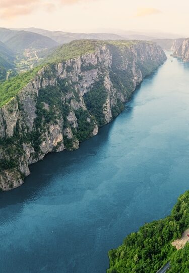 The Danube River carves a dramatic blue path through towering, forest-covered limestone cliffs in Serbia's Iron Gate Gorge