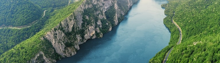 The Danube River carves a dramatic blue path through towering, forest-covered limestone cliffs in Serbia's Iron Gate Gorge