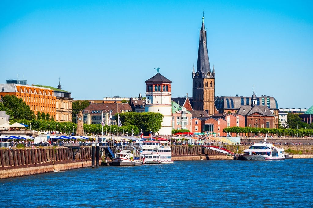 Düsseldorf rise along the sunlit Rhine River promenade in Germany.