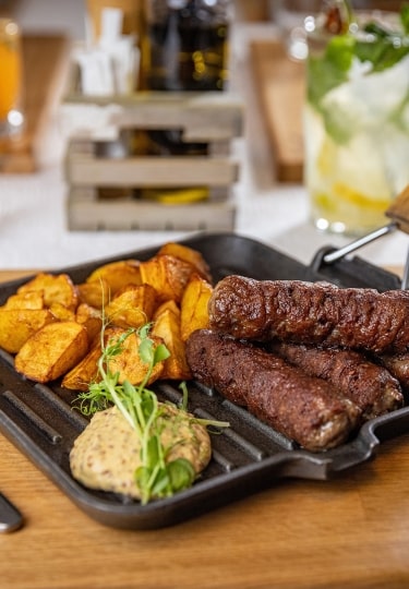 Grilled Romanian mici served with golden roasted potatoes and mustard.