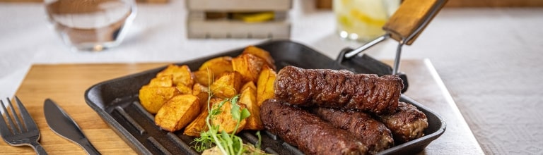 Grilled Romanian mici served with golden roasted potatoes and mustard.