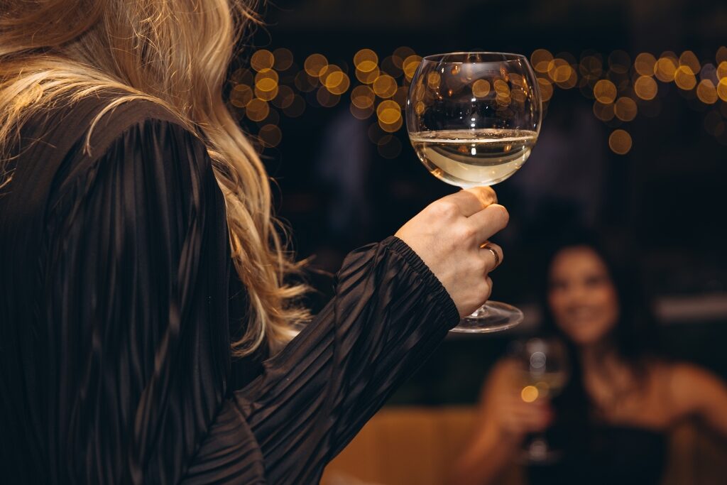 A woman holds up a glass of crisp white wine against a warm, twinkling backdrop of ambient lights in a cozy Budapest ruin bar.