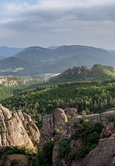 Towering red sandstone Belogradchik Rocks rise above lush green Bulgarian hills.