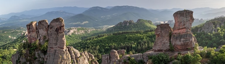 Towering red sandstone Belogradchik Rocks rise above lush green Bulgarian hills.