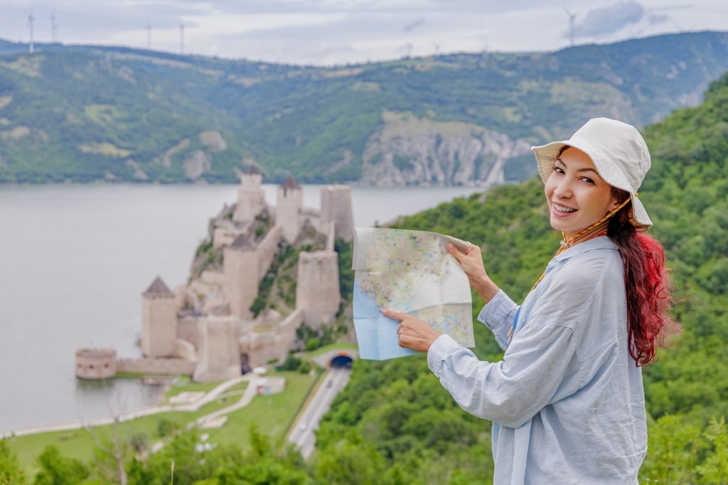 A traveler holds a map while surveying the majestic Golubac stronghold and the shimmering Danube below.