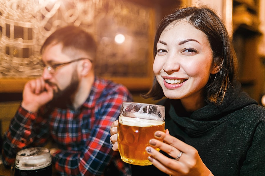 A smiling woman holds a mug of golden, freshly poured Czech lager inside a cozy, dimly lit Prague tavern.