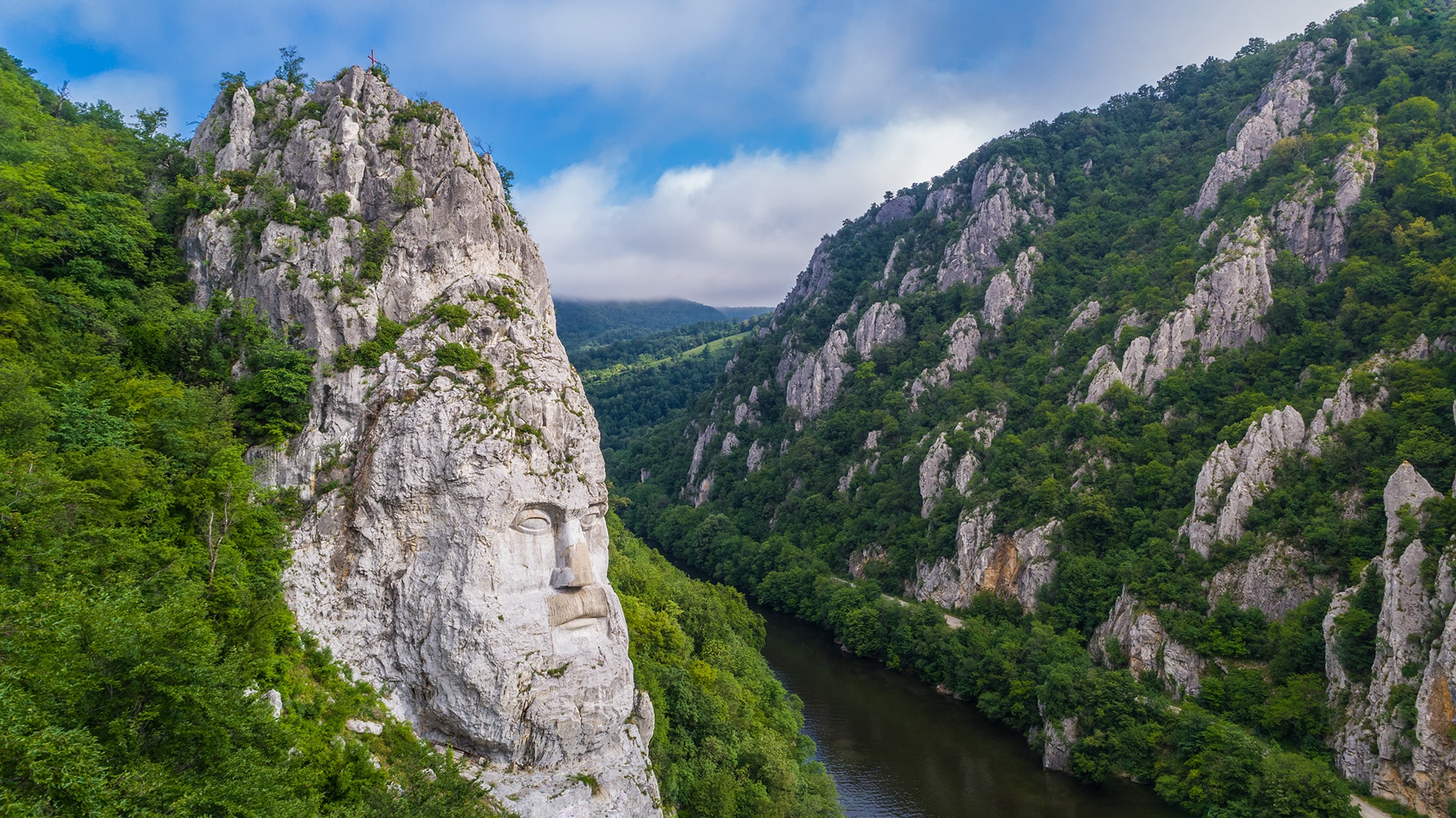 The monumental stone portrait of King Decebalus, chiseled into the towering Romanian cliffs, watches over the verdant depths of the Danube Gorges
