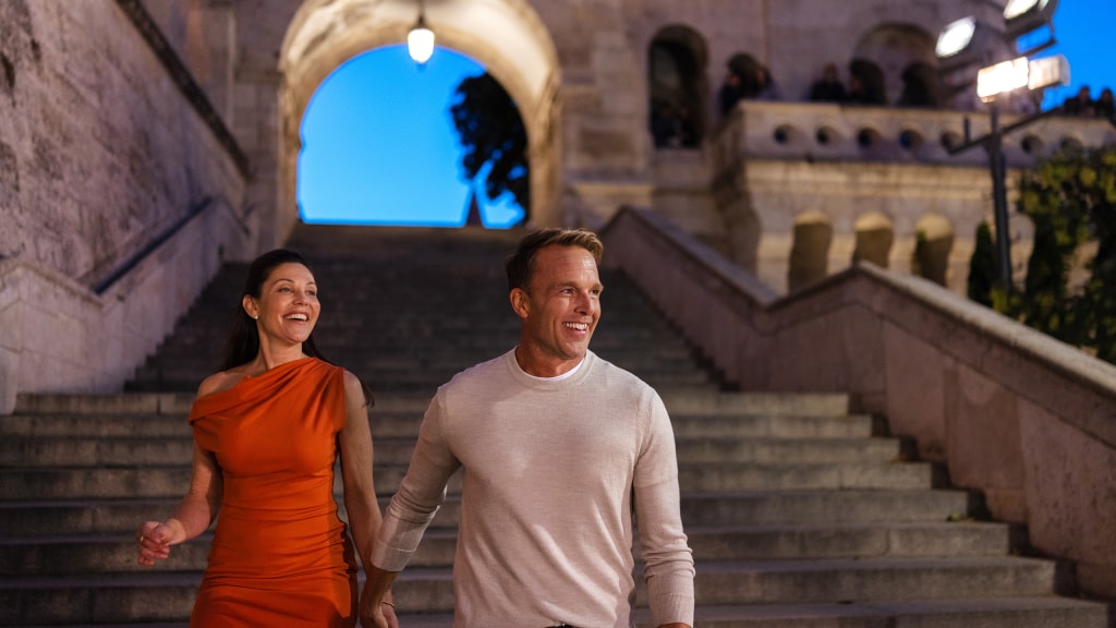 A couple descends the illuminated stone stairs of Budapest’s Fisherman's Bastion.
